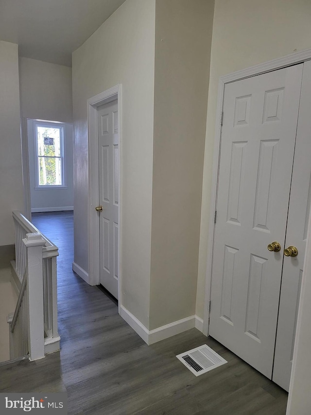 hallway featuring wood finished floors, visible vents, baseboards, and an upstairs landing