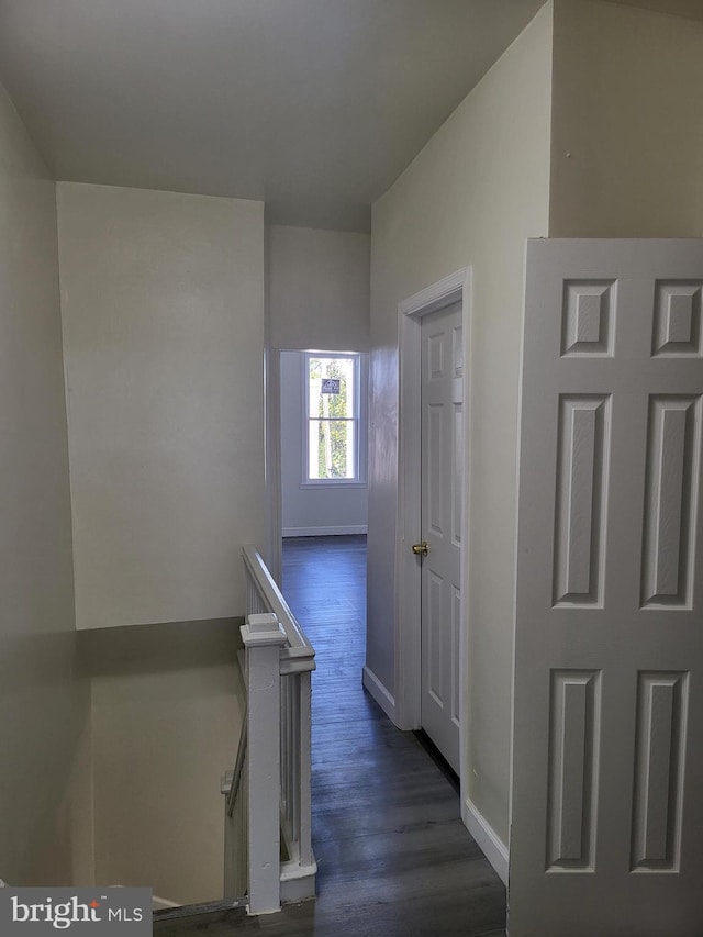 hallway with baseboards, an upstairs landing, and dark wood finished floors