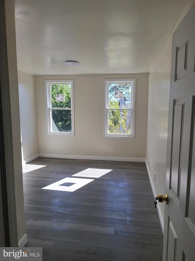 spare room with a wealth of natural light and dark wood-type flooring