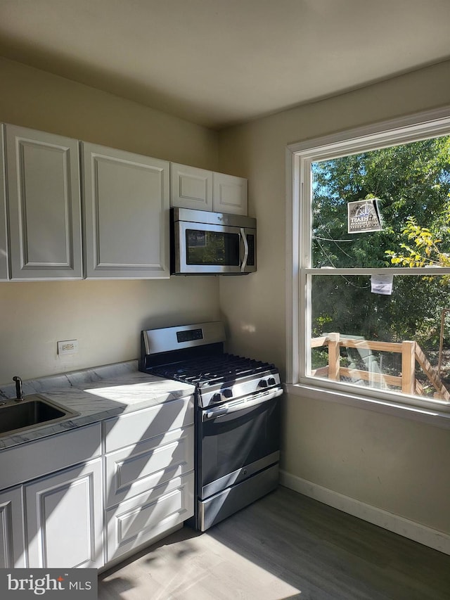 kitchen with stainless steel appliances, white cabinets, hardwood / wood-style flooring, and sink