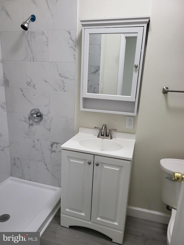 bathroom with wood-type flooring, toilet, vanity, and tiled shower