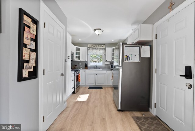 kitchen with white cabinets, stainless steel appliances, light wood-type flooring, and sink