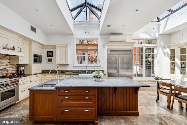 kitchen with a healthy amount of sunlight, a large island with sink, built in appliances, and a skylight