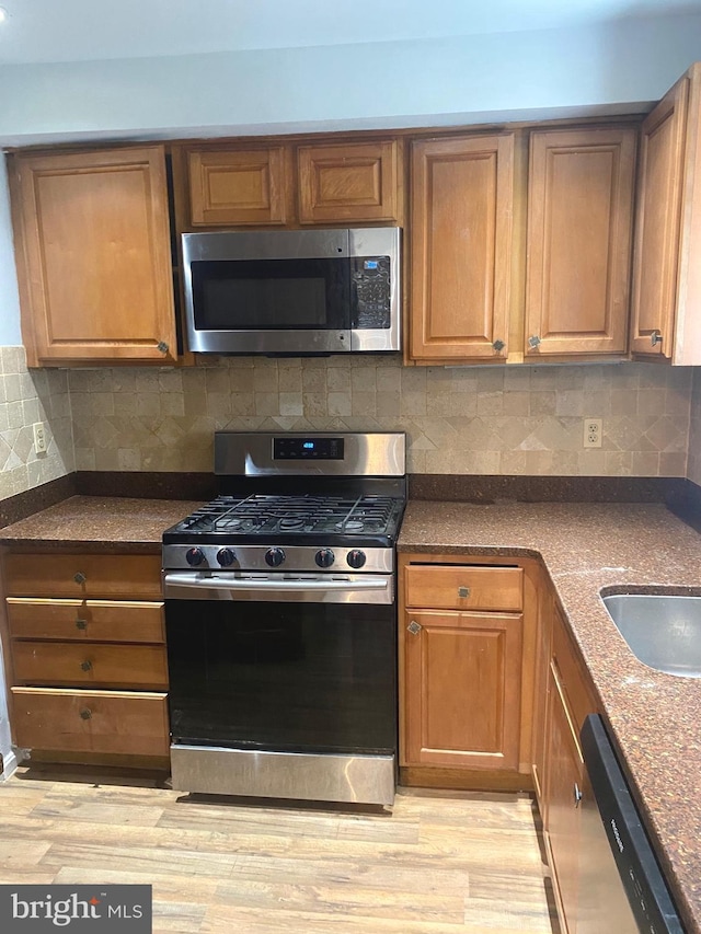 kitchen featuring dark stone counters, light hardwood / wood-style floors, backsplash, and appliances with stainless steel finishes