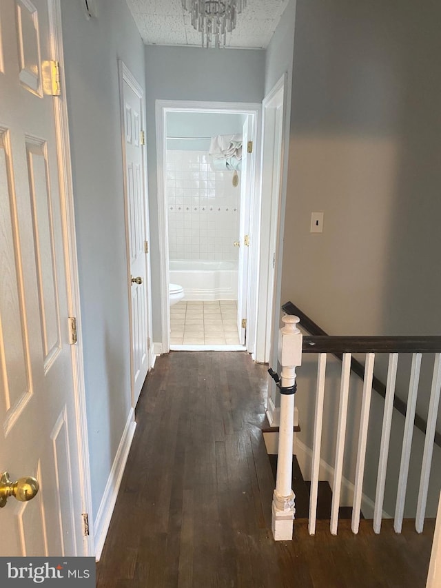 corridor with dark wood-type flooring, a chandelier, and a textured ceiling