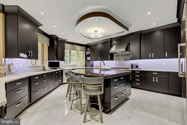 kitchen with decorative backsplash, stainless steel gas cooktop, wall chimney range hood, and a center island with sink