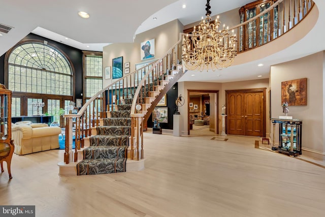 foyer entrance featuring a towering ceiling, an inviting chandelier, and light wood-type flooring