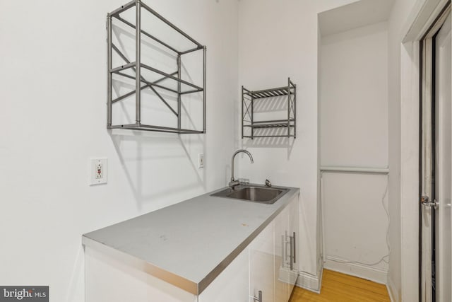 washroom featuring wet bar, light wood-type flooring, baseboards, and a sink