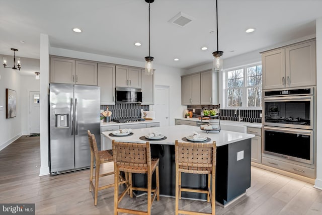 kitchen featuring pendant lighting, light wood-type flooring, a center island, decorative backsplash, and stainless steel appliances