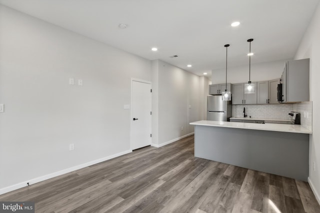 kitchen featuring kitchen peninsula, wood-type flooring, stainless steel refrigerator, gray cabinets, and decorative backsplash