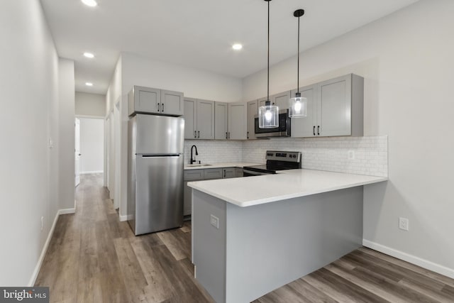 kitchen featuring sink, kitchen peninsula, hanging light fixtures, stainless steel appliances, and dark hardwood / wood-style flooring