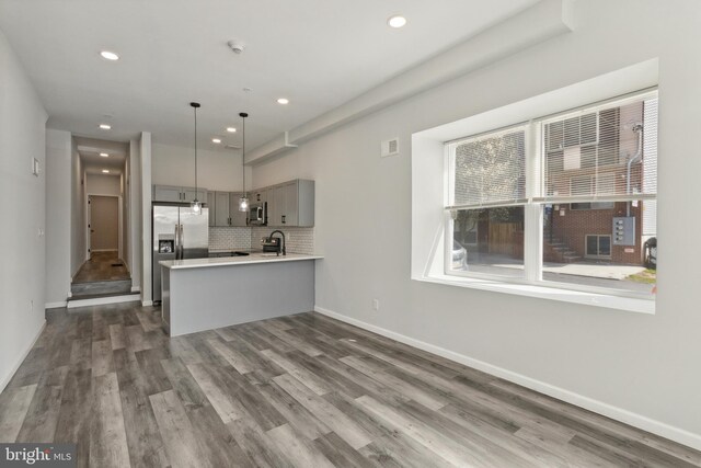 kitchen with pendant lighting, kitchen peninsula, gray cabinetry, appliances with stainless steel finishes, and dark hardwood / wood-style floors