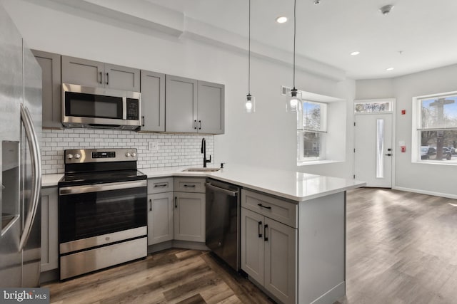 kitchen featuring hanging light fixtures, sink, kitchen peninsula, appliances with stainless steel finishes, and dark hardwood / wood-style flooring