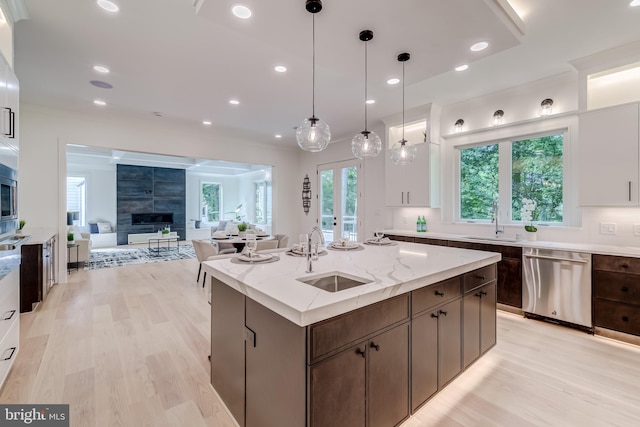 kitchen featuring dishwasher, a kitchen island with sink, hanging light fixtures, a tile fireplace, and sink