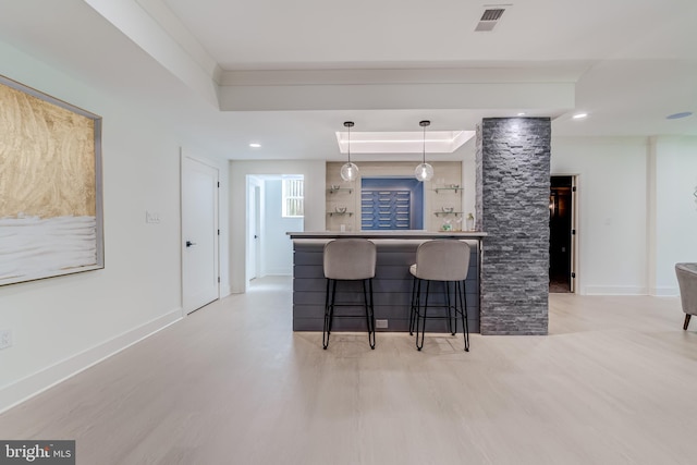 kitchen featuring a kitchen breakfast bar, light hardwood / wood-style flooring, a tray ceiling, and pendant lighting