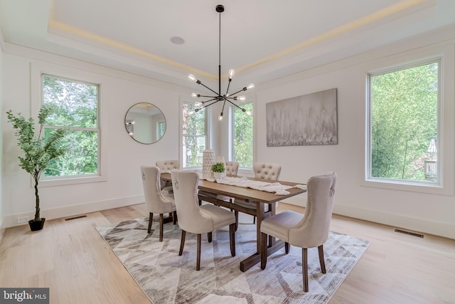 dining space with a chandelier, light hardwood / wood-style floors, and a raised ceiling