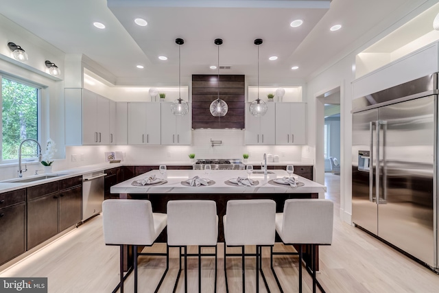 kitchen with a center island with sink, stainless steel appliances, sink, and decorative light fixtures