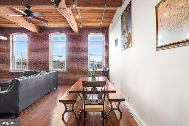 dining space featuring ceiling fan, hardwood / wood-style flooring, brick wall, wood ceiling, and beam ceiling