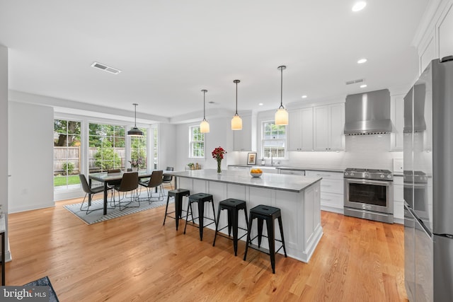 1307 Cleveland St, Alexandria, VA 22302 - kitchen featuring appliances with stainless steel finishes, wall chimney range hood, white cabinets, a center island, and recessed lighting