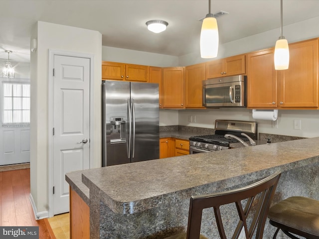 kitchen with pendant lighting, light hardwood / wood-style floors, a breakfast bar area, kitchen peninsula, and appliances with stainless steel finishes