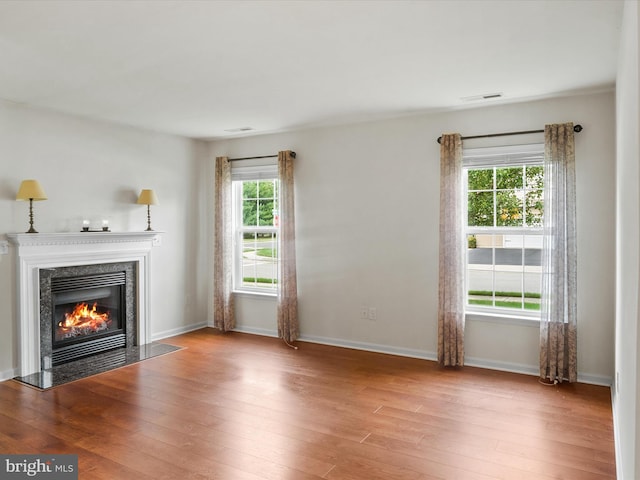 unfurnished living room featuring a healthy amount of sunlight, light hardwood / wood-style flooring, and a premium fireplace