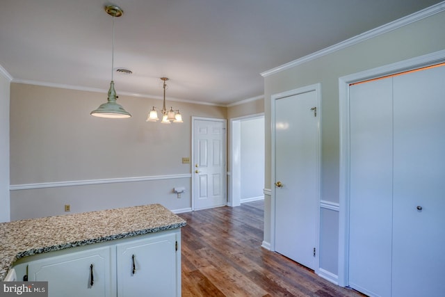 kitchen with dark wood-type flooring, light stone counters, hanging light fixtures, ornamental molding, and white cabinetry