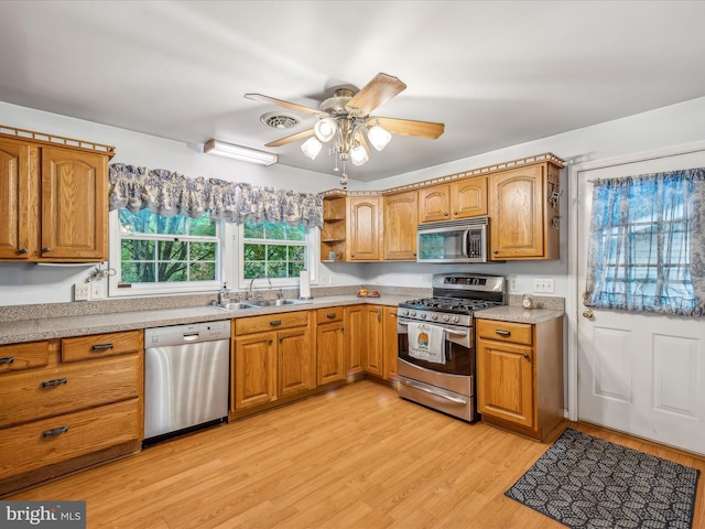 kitchen with appliances with stainless steel finishes, light wood-type flooring, sink, and ceiling fan