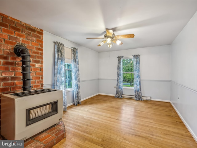 unfurnished living room with heating unit, baseboard heating, a wood stove, ceiling fan, and light hardwood / wood-style flooring