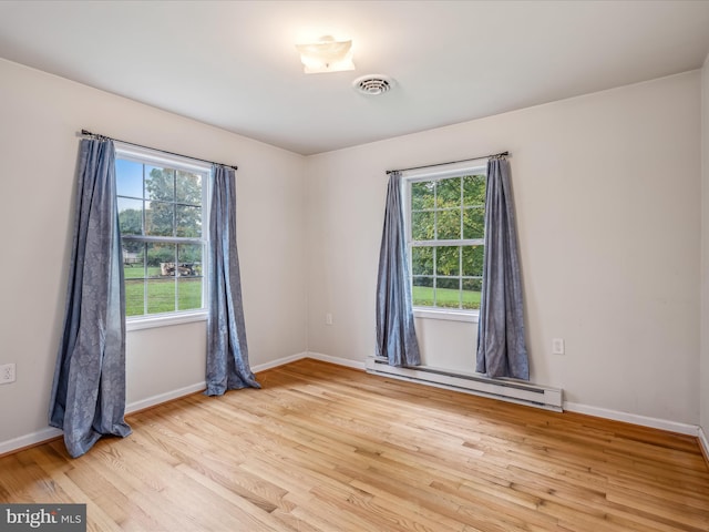 unfurnished room with a baseboard heating unit, light hardwood / wood-style floors, and a wealth of natural light