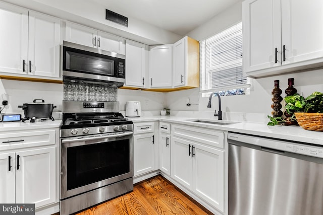 kitchen with light hardwood / wood-style floors, sink, light stone counters, appliances with stainless steel finishes, and white cabinetry