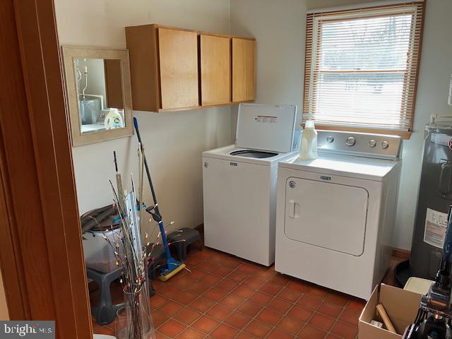 clothes washing area with cabinets, dark tile patterned flooring, electric water heater, and washer and dryer