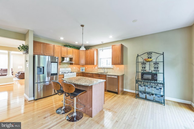 kitchen featuring pendant lighting, a center island, light hardwood / wood-style flooring, appliances with stainless steel finishes, and light stone countertops