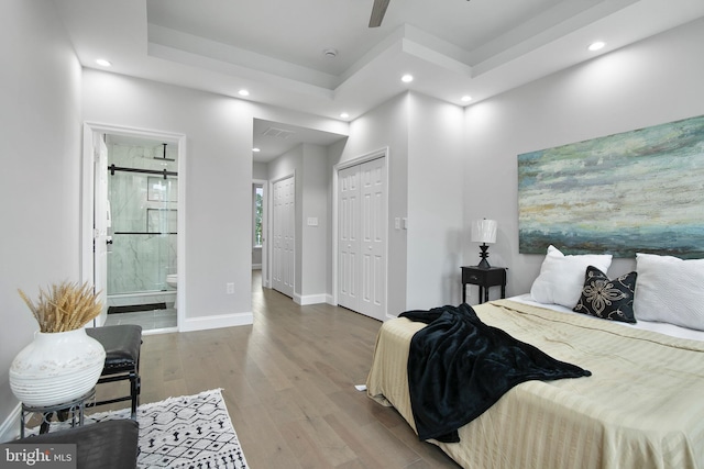 bedroom with a raised ceiling, connected bathroom, ceiling fan, and light hardwood / wood-style flooring