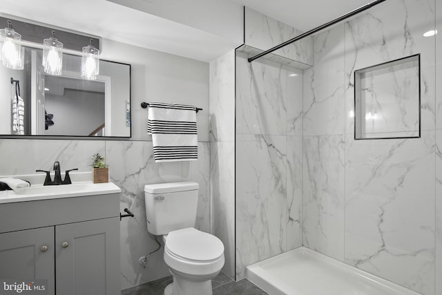 bathroom with tile walls, tiled shower, vanity, and toilet