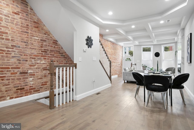 dining room featuring brick wall, light wood-type flooring, beam ceiling, and coffered ceiling