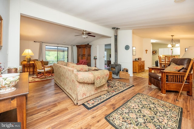 living room with ceiling fan with notable chandelier, light wood-type flooring, lofted ceiling with beams, and a wood stove