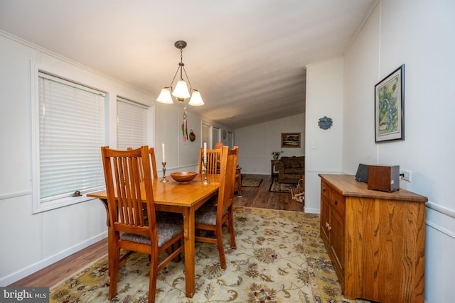 dining space with ornamental molding, an inviting chandelier, light wood-type flooring, and vaulted ceiling