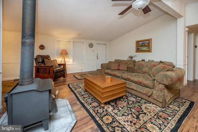 living room featuring lofted ceiling, ceiling fan, a wood stove, and hardwood / wood-style flooring