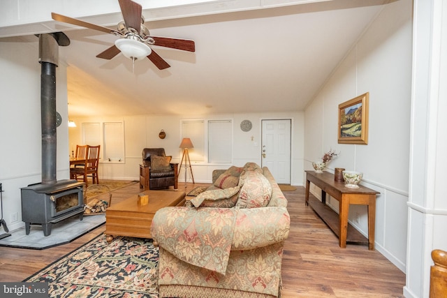 living room with ceiling fan, lofted ceiling, light hardwood / wood-style floors, and a wood stove