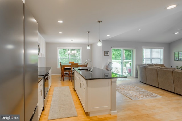 kitchen with hanging light fixtures, a center island with sink, white cabinetry, stainless steel appliances, and light hardwood / wood-style floors