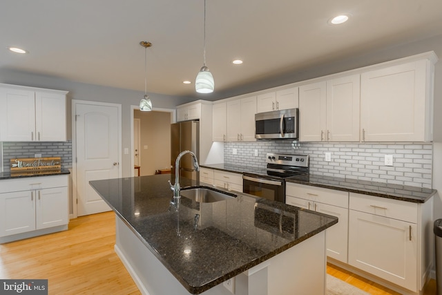 kitchen with sink, white cabinetry, hanging light fixtures, stainless steel appliances, and a center island with sink