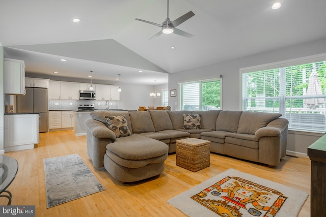 living room featuring ceiling fan with notable chandelier, sink, light hardwood / wood-style flooring, and high vaulted ceiling