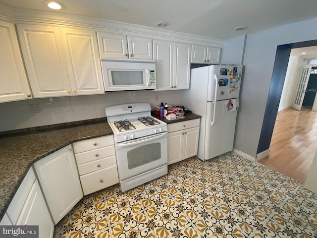 kitchen with decorative backsplash, light hardwood / wood-style floors, white cabinets, white appliances, and dark stone counters