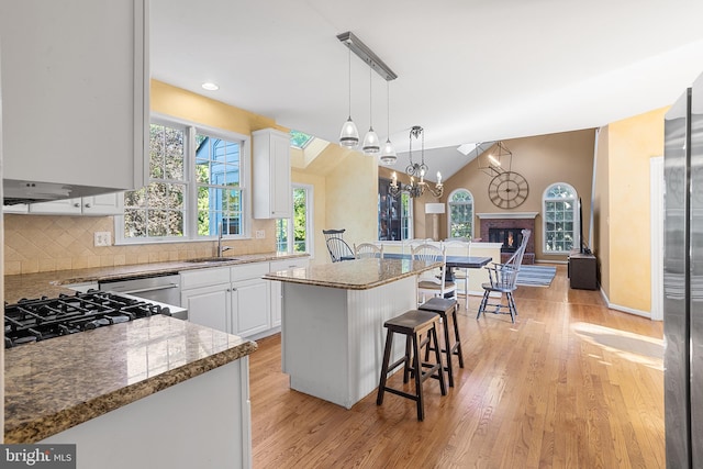 kitchen with a brick fireplace, a center island, a breakfast bar, dark stone countertops, and white cabinetry