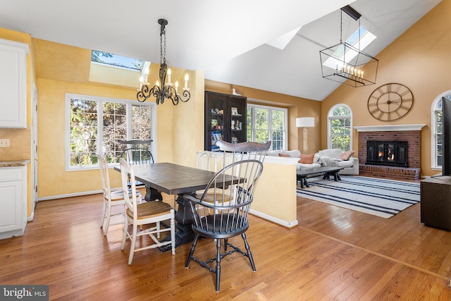 dining area featuring a fireplace, a chandelier, light wood-type flooring, and lofted ceiling with skylight