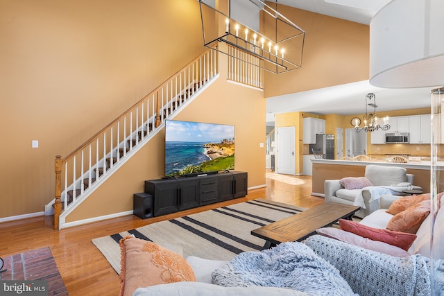 living room featuring light wood-type flooring, a towering ceiling, and an inviting chandelier