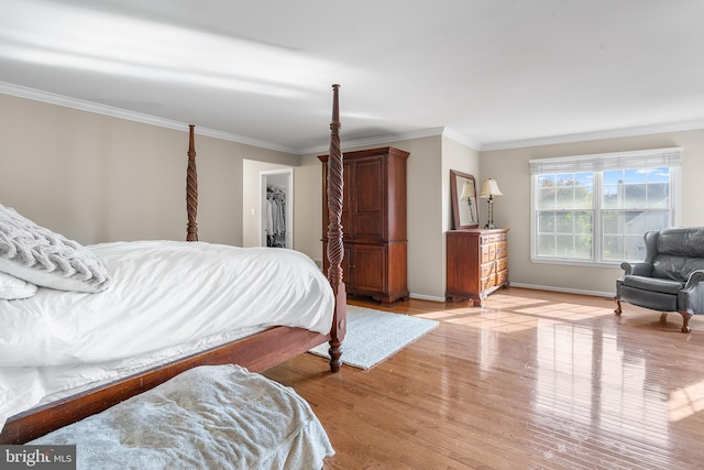 bedroom with a closet, ornamental molding, a walk in closet, and light hardwood / wood-style flooring