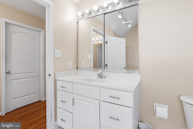 bathroom featuring hardwood / wood-style flooring, vanity, lofted ceiling, and toilet