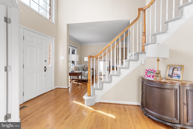 entrance foyer with wood-type flooring, crown molding, and a towering ceiling