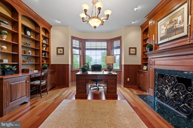 office area with built in shelves, an inviting chandelier, light wood-type flooring, and wooden walls